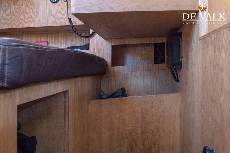 Een interieur van een boot met houten wanden, een bruin kussen, een zwart apparaat en een opgerolde kabel. — Tradewind 35