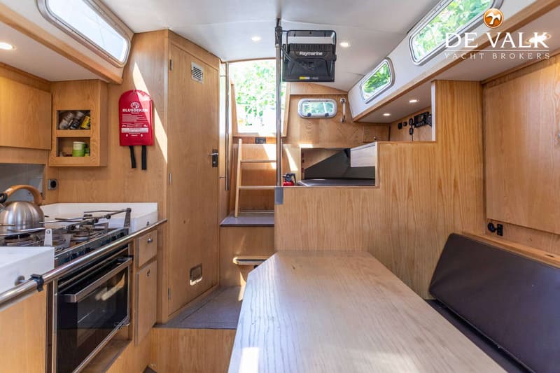 De foto toont het interieur van een boot met een kombuis, een tafel, een bank en een trap naar de uitgang. — Tradewind 35