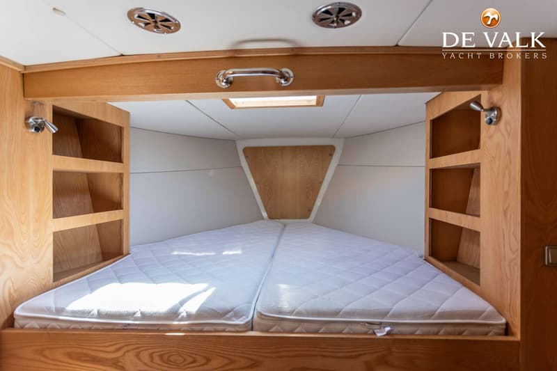 Een kajuit met een V-vormig bed met twee matrassen, houten kasten aan de zijkanten en een dakraam. — Tradewind 35