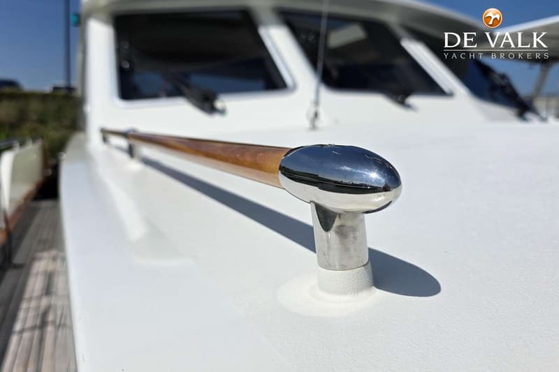 Een detail van een witte boot met een houten handreling en chromen bevestigingen, met een "DE VALK YACHT BROKERS" logo.