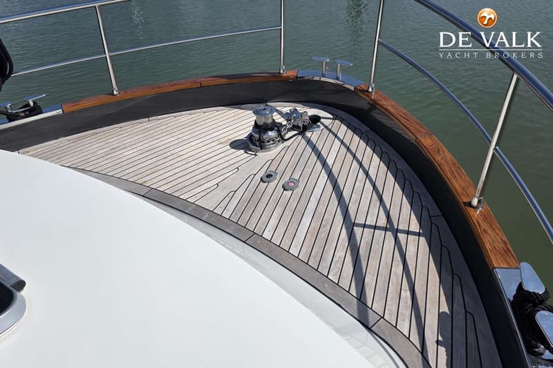 De foto toont het voordek van een boot met een houten dek, een ankerlier en een reling. — Linssen 450 Range Cruiser Sedan