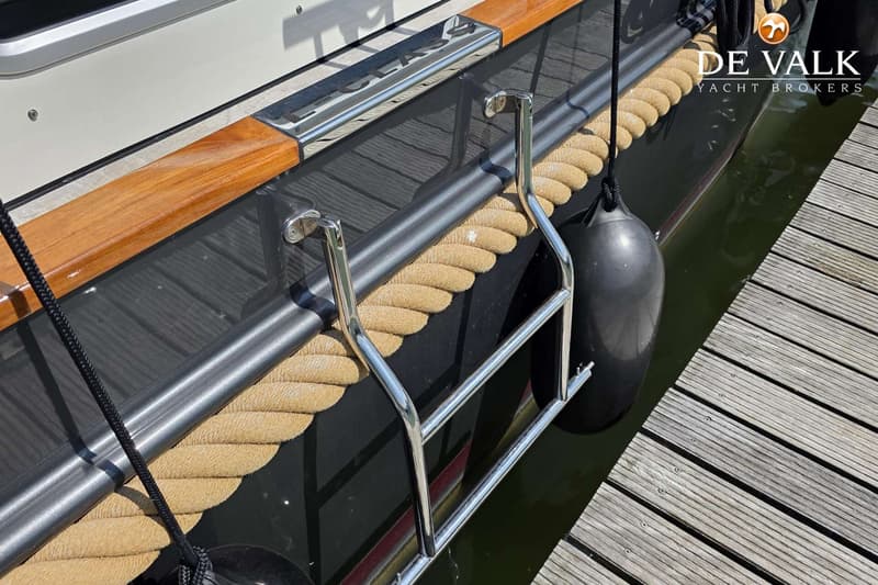 Een boot met een touwstootrand, een zwemtrap en een zwarte fender, liggend aan een houten steiger.