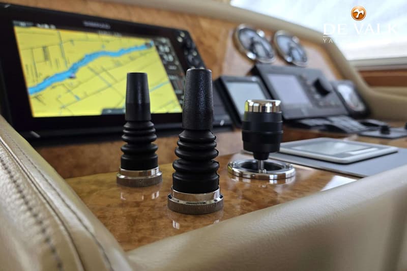 Drie zwarte joysticks met chromen details staan op een houten dashboard, met een navigatiescherm op de achtergrond.