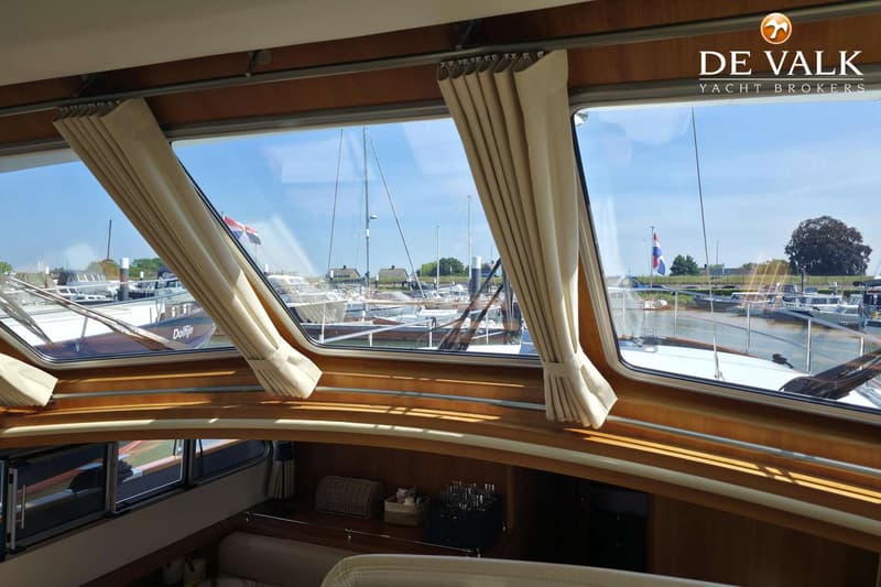 Een interieurfoto van een boot met uitzicht op een jachthaven, met houten afwerking en crèmekleurige gordijnen.