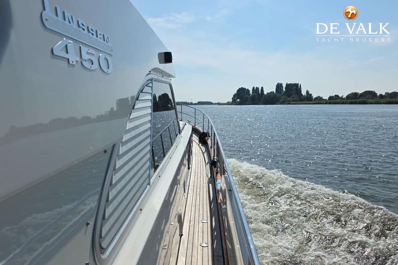 Een witte boot met "LINSSEN 450" op de zijkant vaart over water, met een houten dek en reling zichtbaar.