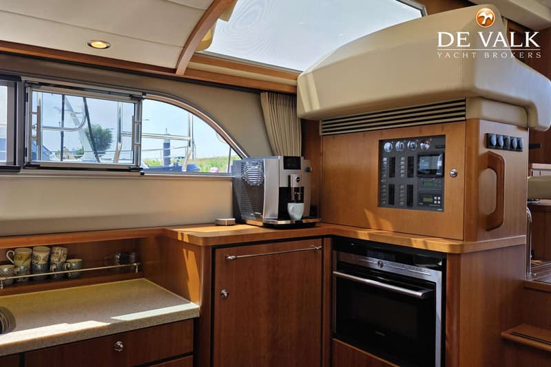 Een interieur van een boot met een koffiezetapparaat, een oven, een bedieningspaneel en een raam met uitzicht naar buiten.