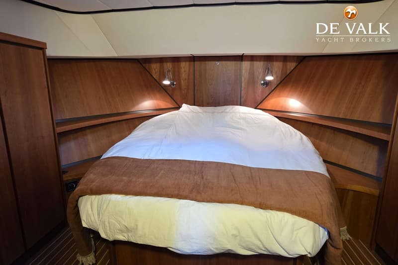 Een kajuit met een tweepersoonsbed, houten wanden en vloer, en twee leeslampjes boven het bed.