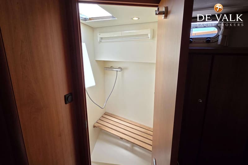 Een interieurfoto van een doucheruimte met een houten bankje, een douchekop en een dakraam.