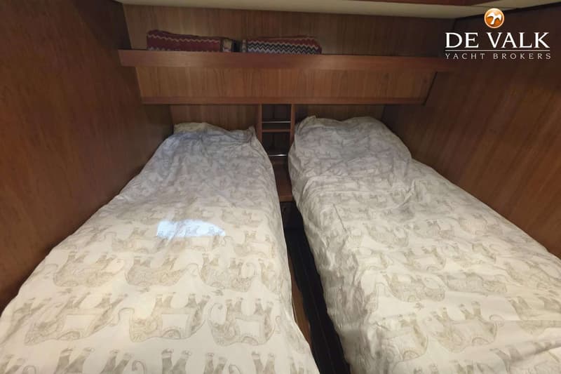Twee bedden met witte dekbedden met olifantenpatroon, gescheiden door een houten nachtkastje, in een houten kajuit.