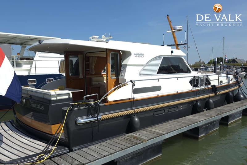 Een witte en donkergrijze boot, met de naam "Zwartsluis" en "Linssen 450", ligt afgemeerd aan een houten steiger.