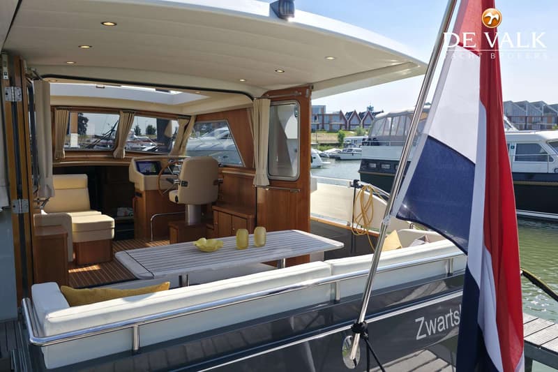 Een boot met een Nederlandse vlag, een stuurhut met houten interieur en een zithoek met tafel.
