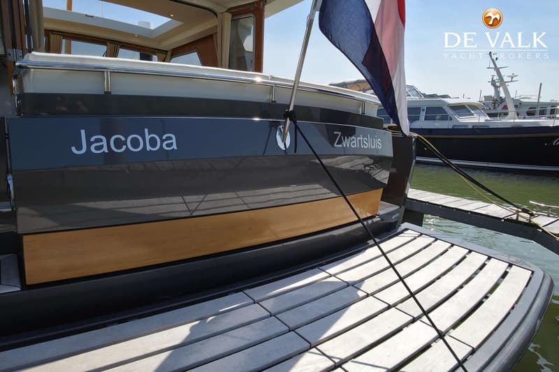 De achtersteven van een boot met de naam "Jacoba" en de thuishaven "Zwartsluis" is zichtbaar, met een Nederlandse vlag en…