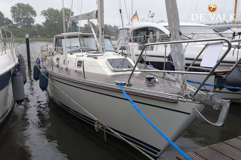 Een zeilboot met een crème romp en een houten dek ligt afgemeerd aan een steiger, met een anker aan de boeg. — LM 35 Vitesse