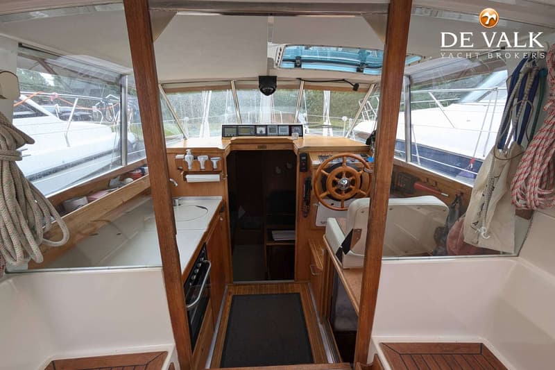 Een interieur van een boot met een houten stuurwiel, een kombuis en een doorgang naar een kajuit. — LM 35 Vitesse