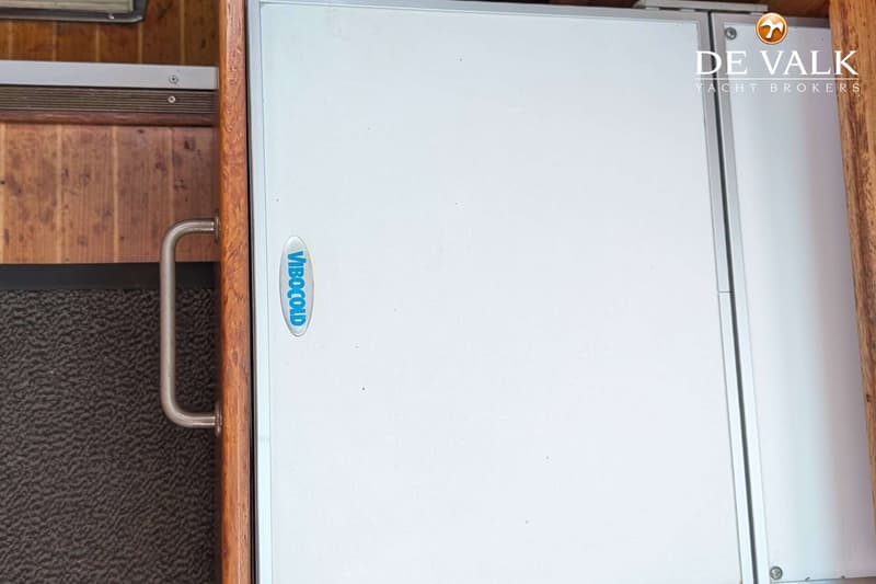 Een witte koelkast of vriezer met het blauwe "VIBOCOLD" logo is zichtbaar, naast een houten wand en een handvat.
