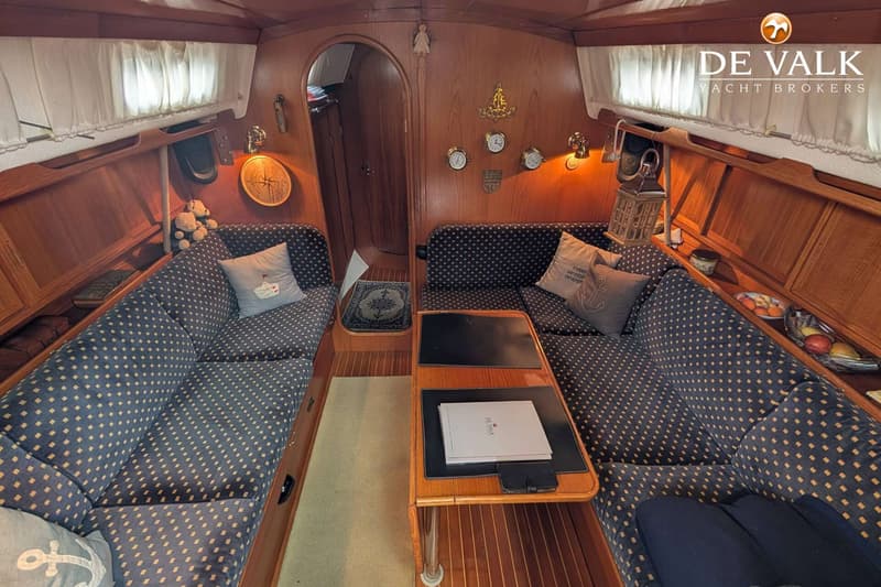 De foto toont het interieur van een boot met houten wanden, twee banken met donkerblauwe kussens en een tafel in het midden.