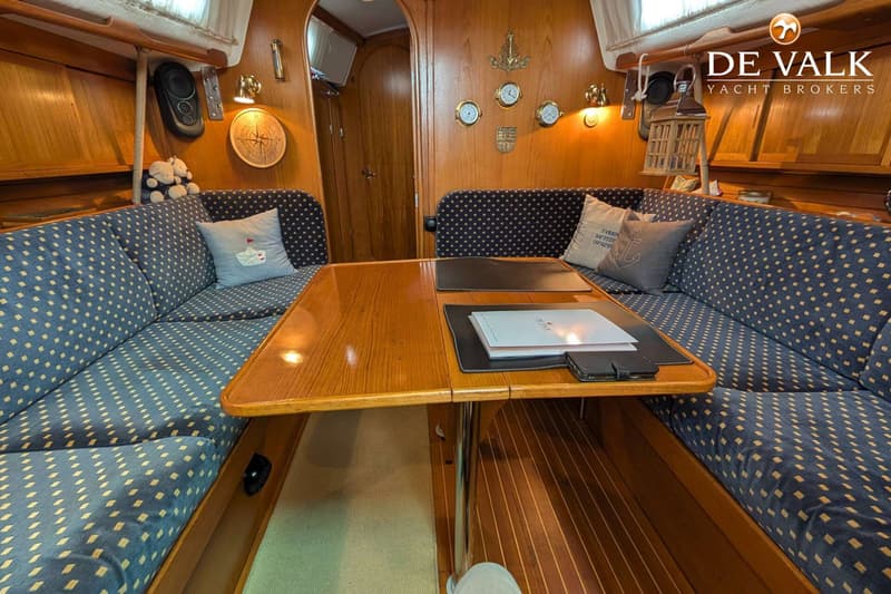 De foto toont het interieur van een boot met een houten tafel en twee banken met blauwe kussens met gele stippen.