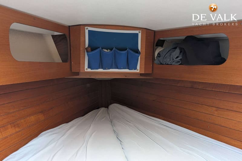 De foto toont het interieur van een boot met houten lambrisering, een wit plafond, twee bedden met witte lakens en…