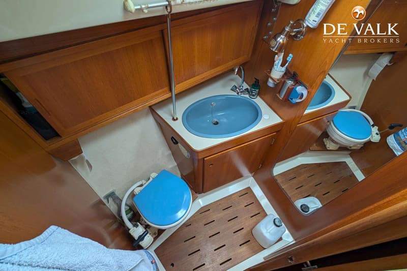 Een badkamer op een boot met een blauwe wasbak, een blauw toilet en houten kasten en vloer. — LM 35 Vitesse