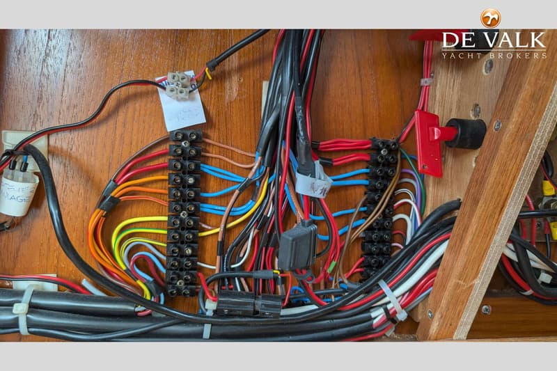 Een close-up van een houten paneel met een wirwar van gekleurde elektrische draden, klemmenstroken en zekeringen.