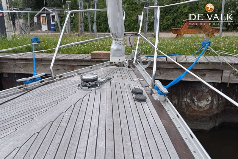 De foto toont het voordek van een zeilboot met een teakdek, een ankerlier, een opgerold zeil en relingen. — LM 35 Vitesse