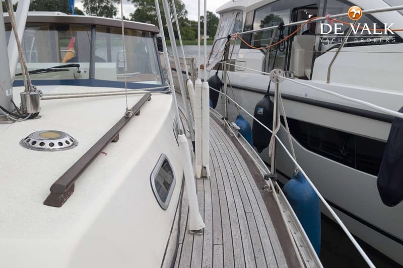 Een boot met een teakhouten dek en een witte romp ligt afgemeerd naast een andere boot, met stootwillen ertussen.