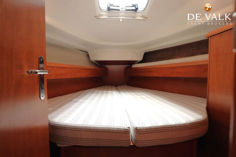 Een interieurfoto van een bootkajuit met een V-vormig bed met gestreepte matrassen, houten wanden en een dakluik.