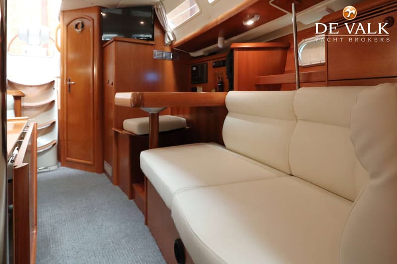 De foto toont het interieur van een boot met een lichte bank, een houten tafel en houten kasten. — Jeanneau Sun Odyssey 37