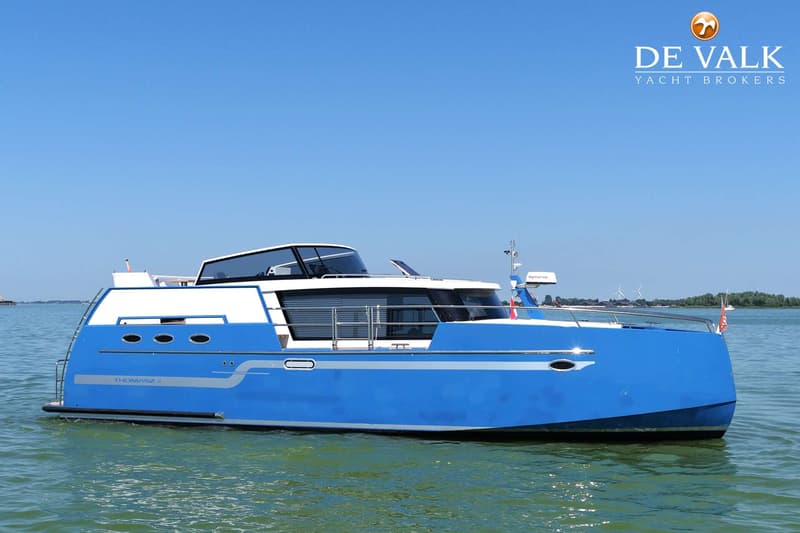 Een blauw-witte motorboot met de naam "THOMASZ 4" is te zien op het water onder een helderblauwe lucht.