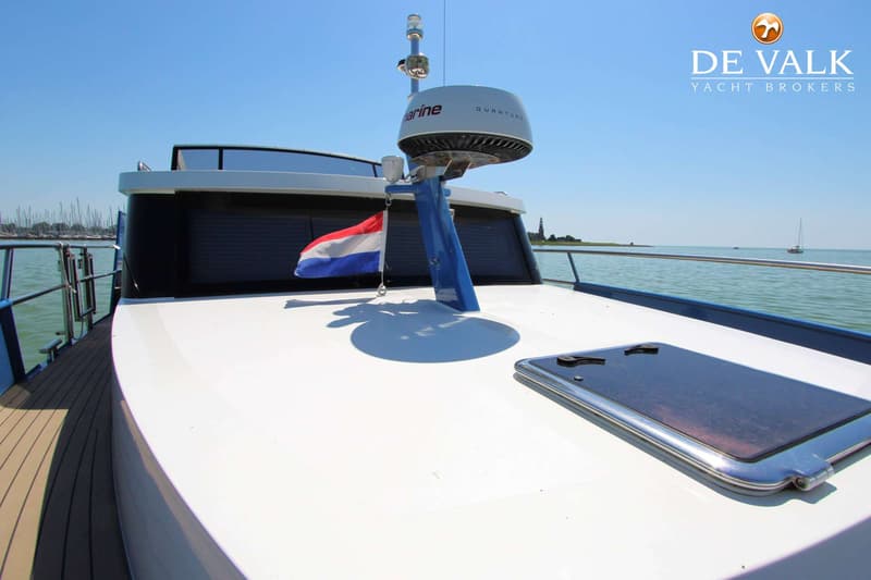 Een witte boot met een radar en een Nederlandse vlag, varend op helder water met een blauwe lucht. — Thomasz Yacht 412 AC