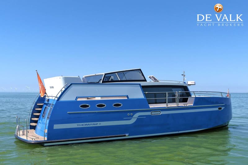 Een blauw-witte motorboot met de naam "THOMASZ 41" ligt in het water onder een helderblauwe lucht. — Thomasz Yacht 412 AC
