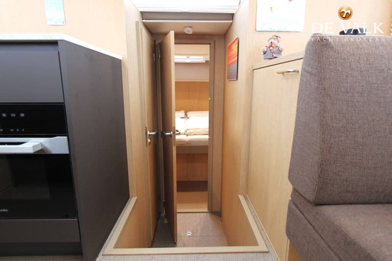 Een interieur van een boot met een open deur naar een slaapgedeelte, een keukenblok met oven en een bank.