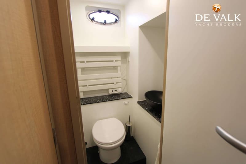 Een witte toiletruimte met een wit toilet, een zwarte waskom, een handdoekrek en een patrijspoort.