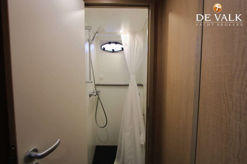 Een douchecabine met een douchekop, een witte douchegordijn, een patrijspoort en een donkere vloer.