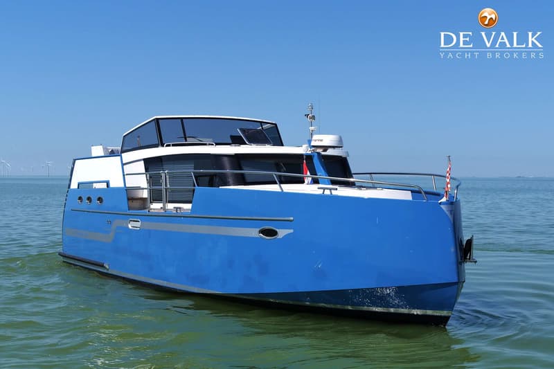 Een blauw-witte motorboot vaart op open water onder een helderblauwe lucht, met windmolens op de achtergrond.