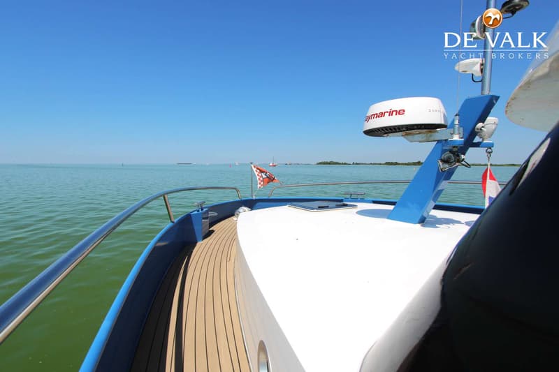 Een boot met een houten dek en een witte opbouw vaart op een water met een blauwe reling en een radar. — Thomasz Yacht 412 AC