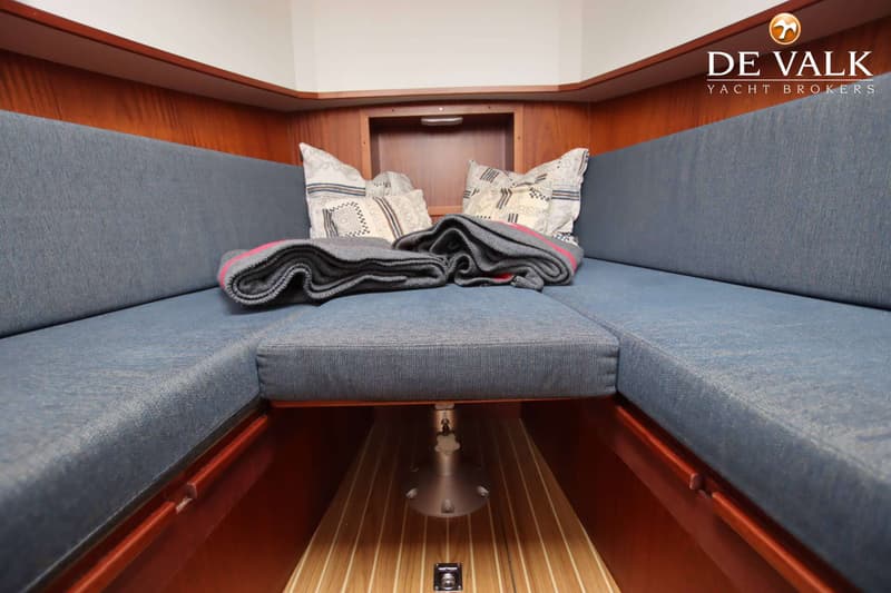 Een interieur van een boot met een U-vormige bank met blauwe kussens, twee sierkussens en een opgevouwen deken.