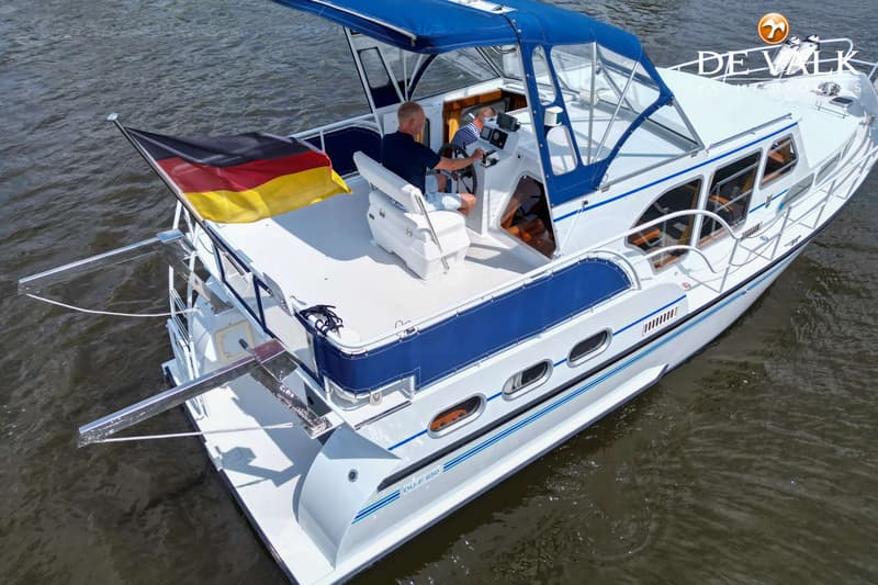 Een witte motorboot met blauwe accenten en een Duitse vlag vaart op het water, met twee mannen aan boord. — Pedro Skiron 35