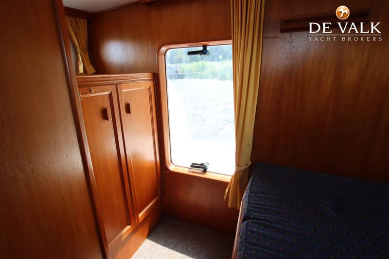 Een interieur van een boot met houten wanden, een raam met uitzicht op water, een kast en een bed met blauw matras.