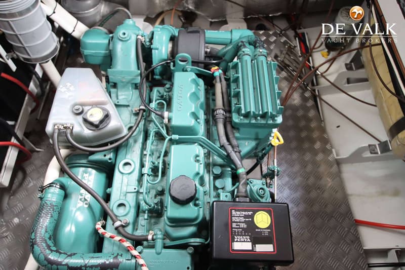 Een Volvo Penta scheepsmotor is zichtbaar, met diverse slangen en kabels, en een metalen vloerplaat.