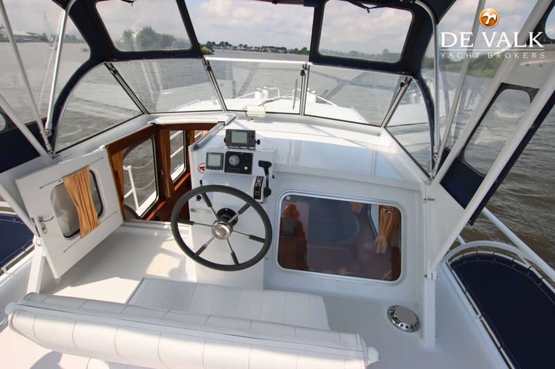 De foto toont de stuurstand van een boot met een stuurwiel, navigatie-instrumenten en een witte bank. — Pedro Skiron 35