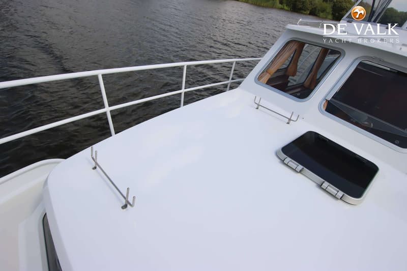 De foto toont het voordek van een witte boot met een reling, ramen en een luik, varend op donker water. — Pedro Skiron 35