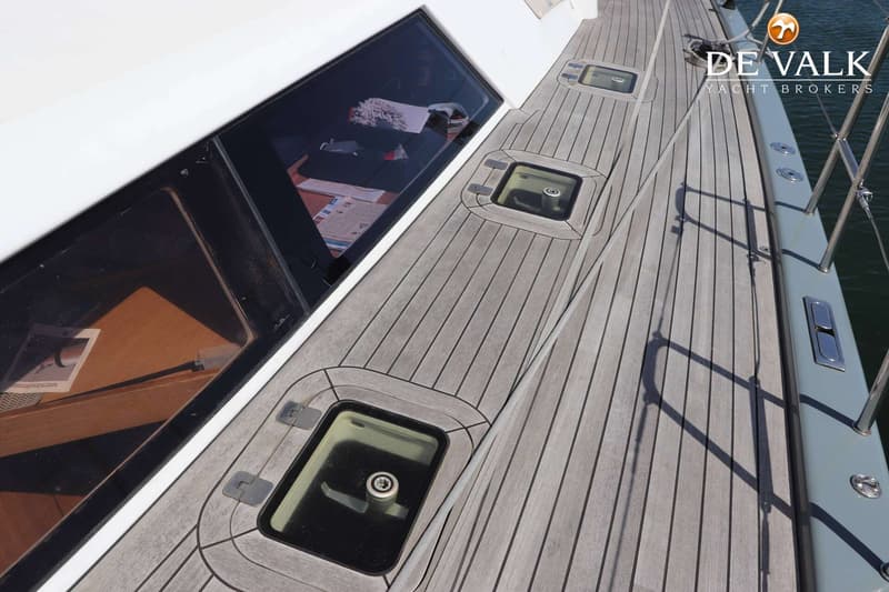Een bovenaanzicht van het teakhouten dek van een boot met twee luiken en een langwerpig raam, met het logo "DE VALK YACHT…