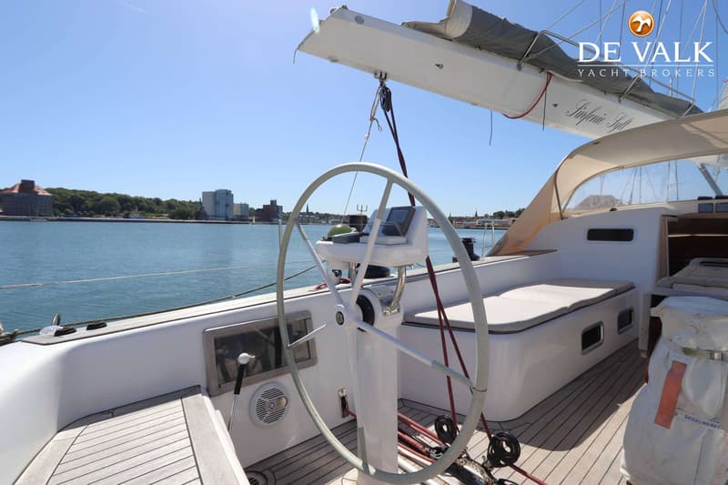 Een stuurwiel en instrumentenpaneel op een zeilboot, met een waterlichaam en gebouwen op de achtergrond. — Grand Soleil 70