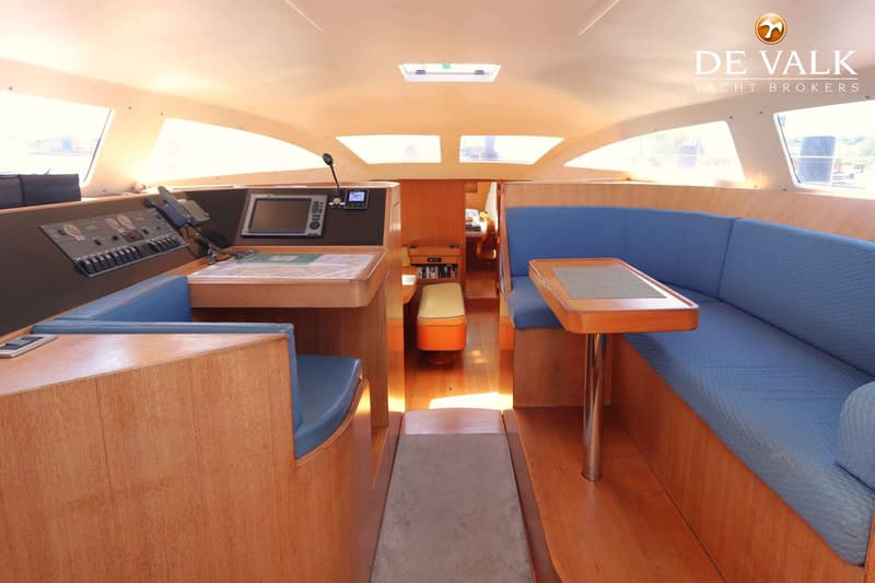 De foto toont het interieur van een boot met houten afwerking, blauwe banken, een tafel en navigatieapparatuur.