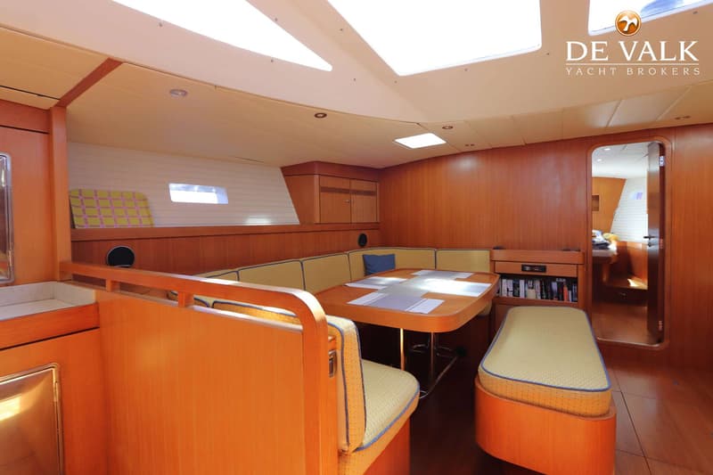 Een interieur van een boot met houten wanden en een tafel omringd door zitbanken met gele kussens. — Grand Soleil 70
