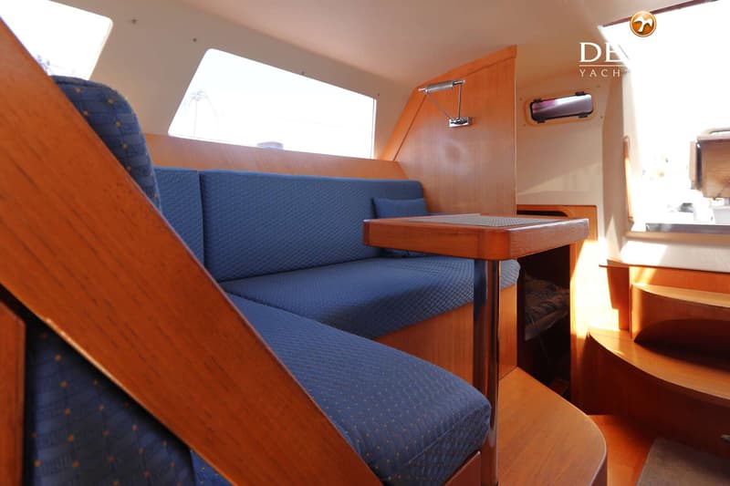 De foto toont een interieur van een boot met blauwe kussens, houten afwerking, een tafel en een trap. — Grand Soleil 70