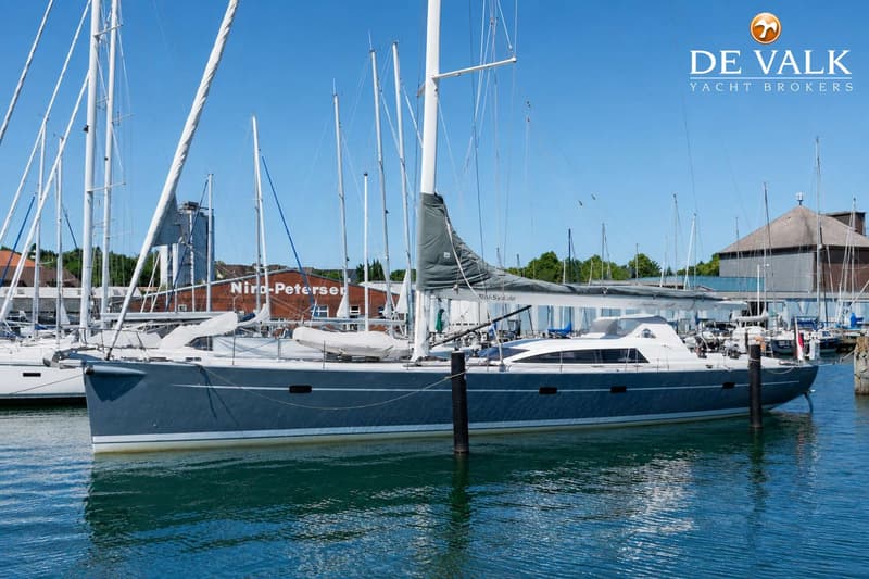 Een grijze zeilboot ligt aangemeerd in een haven met andere boten en gebouwen op de achtergrond. — Grand Soleil 70