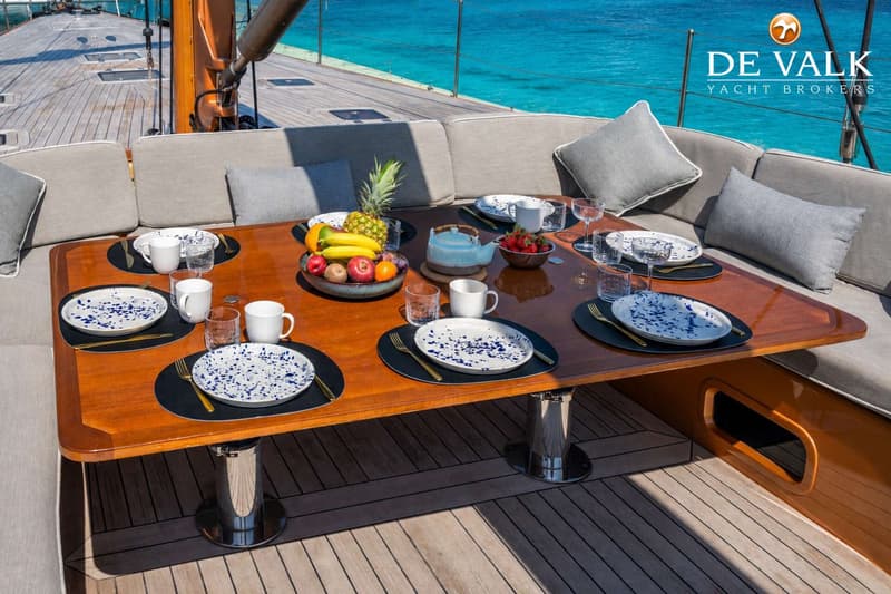 Een gedekte tafel met servies, bestek en fruit staat op het dek van een boot met blauw water op de achtergrond. — Wally 88