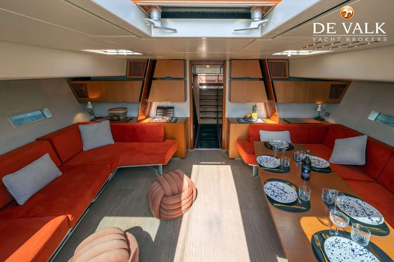 De foto toont het interieur van een boot met een salon, twee oranje banken, een eettafel en een trap naar beneden. — Wally 88